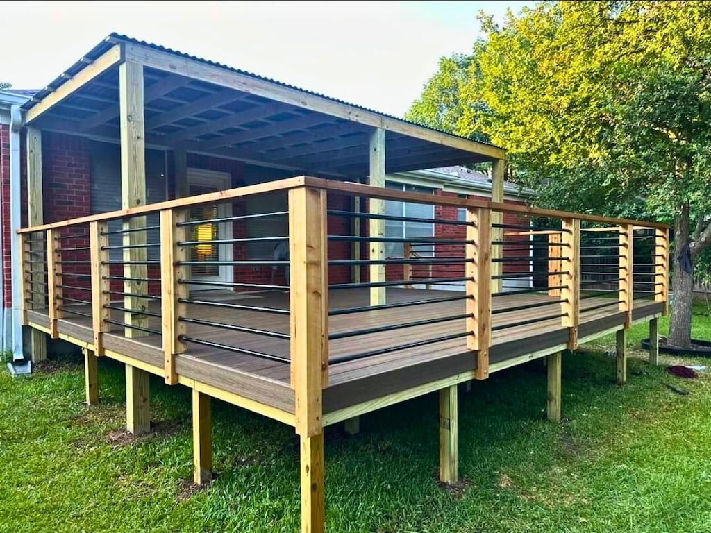 deck-installation-lakeway elevated wooden deck with metal railings, attached to a brick house. The deck is covered, overlooking a grassy yard with a sunlit tree nearby.