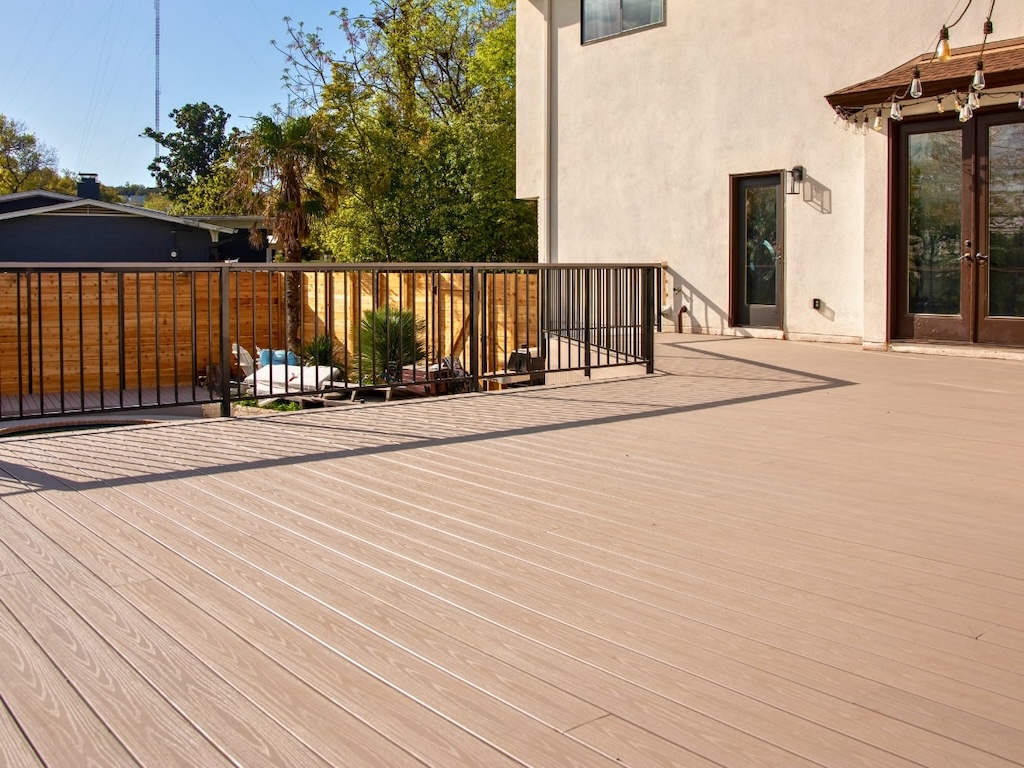 deck-installation-lakeway pacious backyard deck with light wood flooring, metal railing, and wooden privacy fence. Sunlit with garden chairs, plants, and a cozy, inviting ambiance.