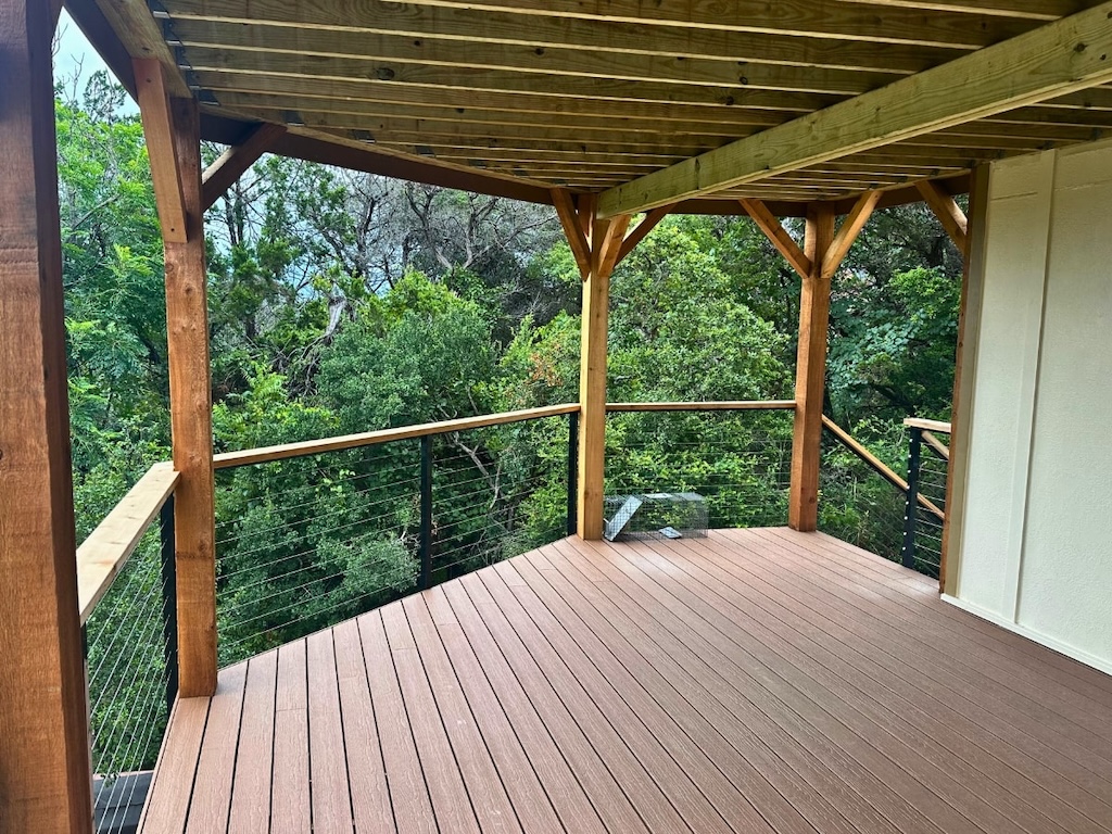 covered wooden deck with railing, overlooking lush green trees. The scene conveys tranquility and offers a peaceful outdoor space amidst nature.